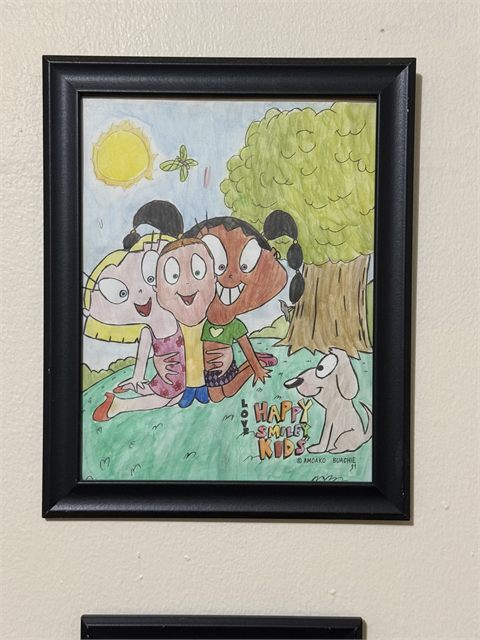 A framed drawing of three cartoon characters sitting together on grass beneath a yellow sun and a small tree.