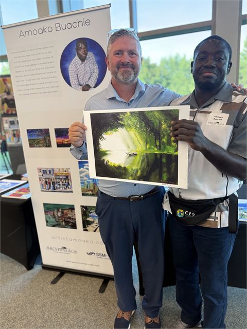 Amoako Buachie holding a framed print of one of his landscape paintings at Archipelago 2026.