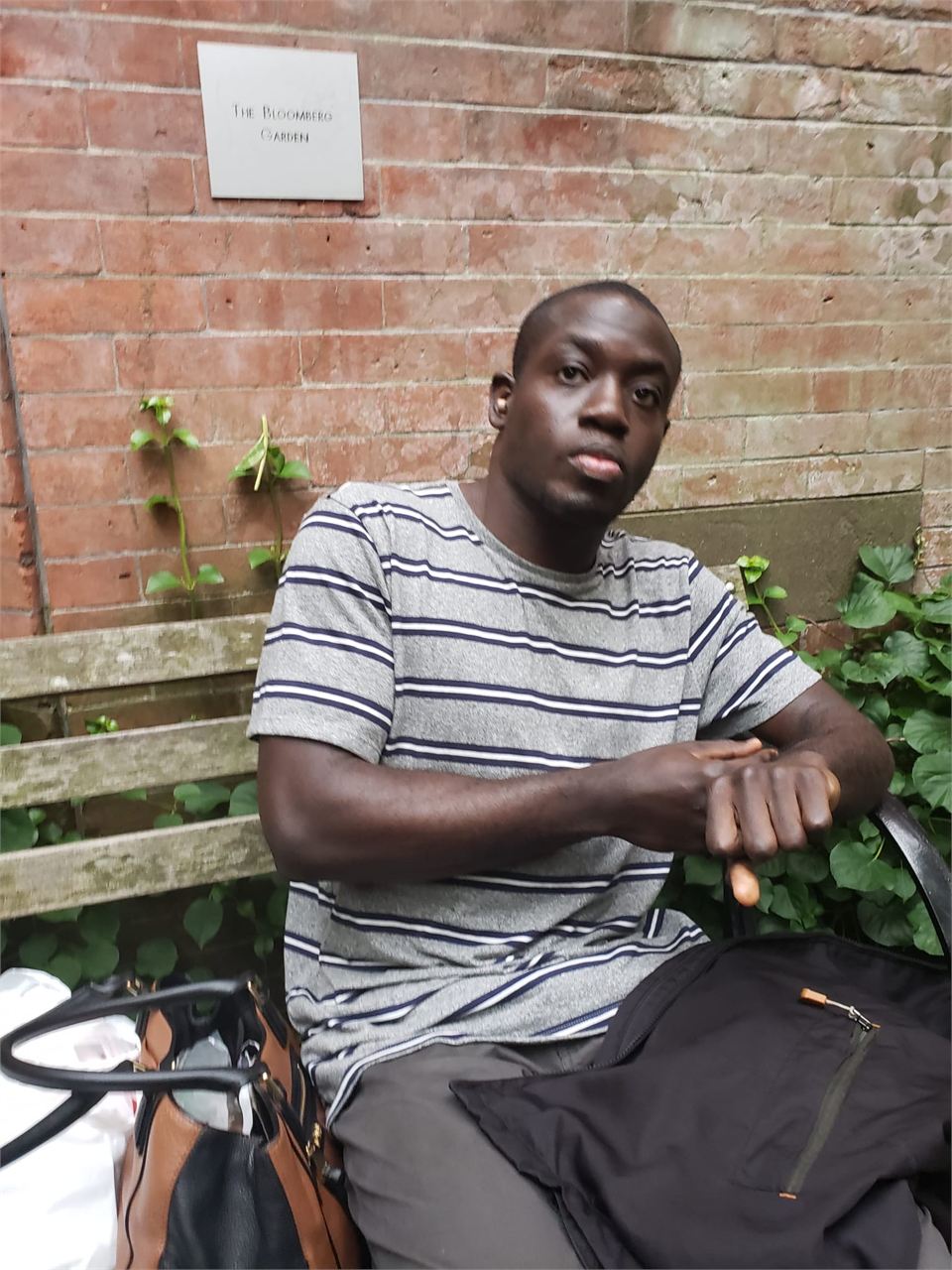Amoako Buachie sitting on a stoop in front of an ivy-covered brick wall, wearing a striped shirt.