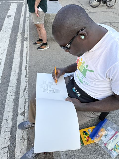 Amoako Buachie sitting on stone steps outdoors, drawing in a large sketchbook.