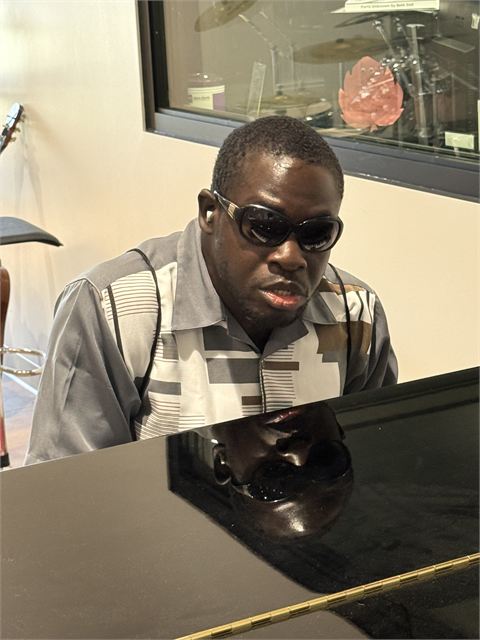 Amoako Buachie seated at a grand piano, hands raised above the keys.