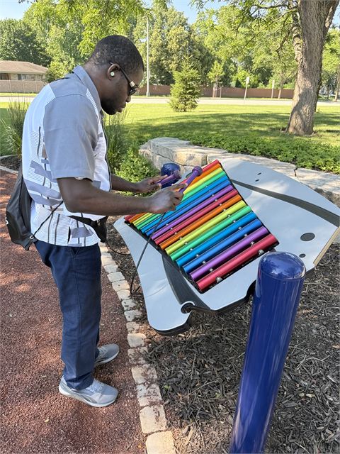 Amoako Buachie playing a brightly coloured outdoor public piano on a sunny day.