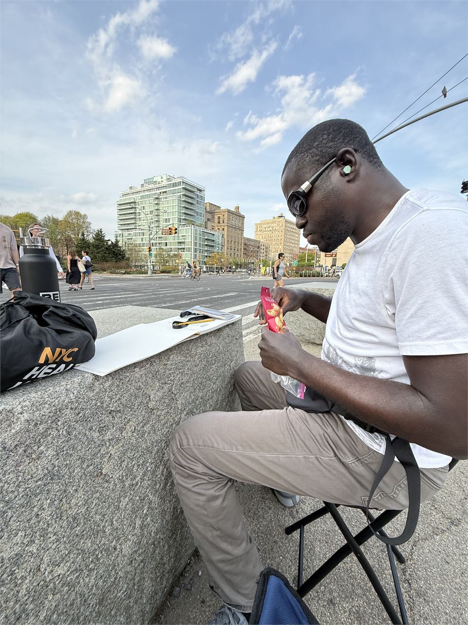 Amoako Buachie crouched beside a canvas on a rooftop, mixing paint with the city skyline behind him.
