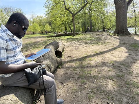 Amoako Buachie painting at a portable easel at the edge of a pond, surrounded by trees.
