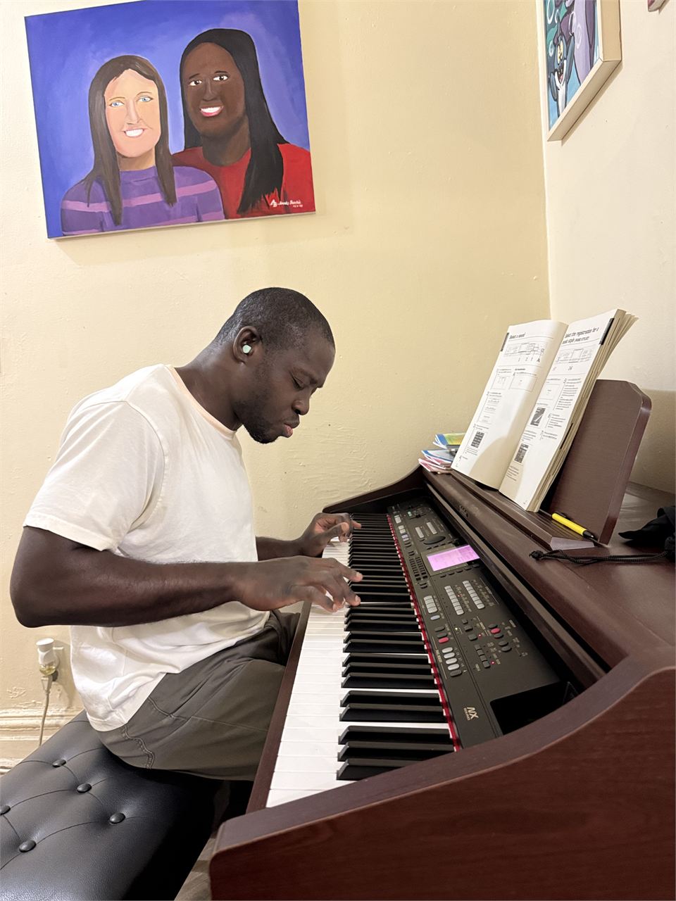 Amoako Buachie playing a piano at home, with one of his paintings hanging on the wall behind him.