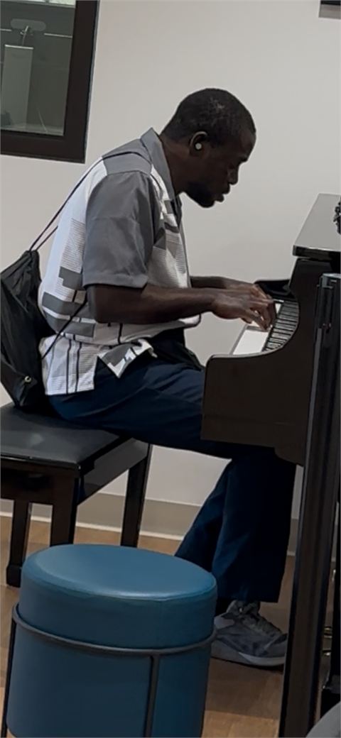 Amoako Buachie practising at an upright piano, seated on a round stool.