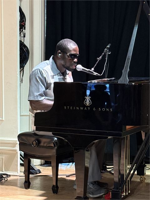 Amoako Buachie singing into a studio microphone beside a piano.
