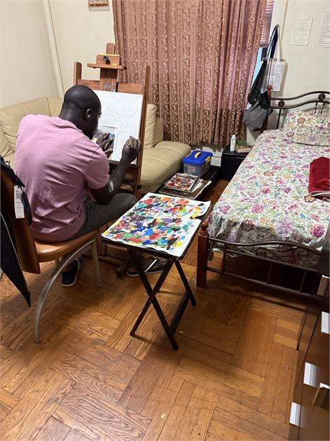 A corner of Amoako Buachie's home studio with a wooden easel, a work in progress and paints laid out on the floor.